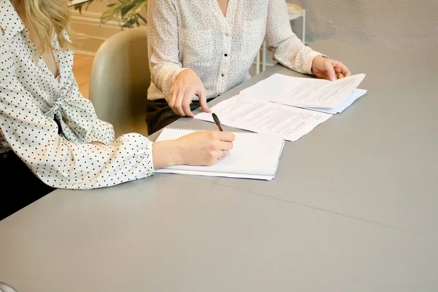 Woman signing documents beside another woman reaching for them