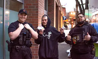 Two security officers posing with a man in a hooded sweatshirt on a city street